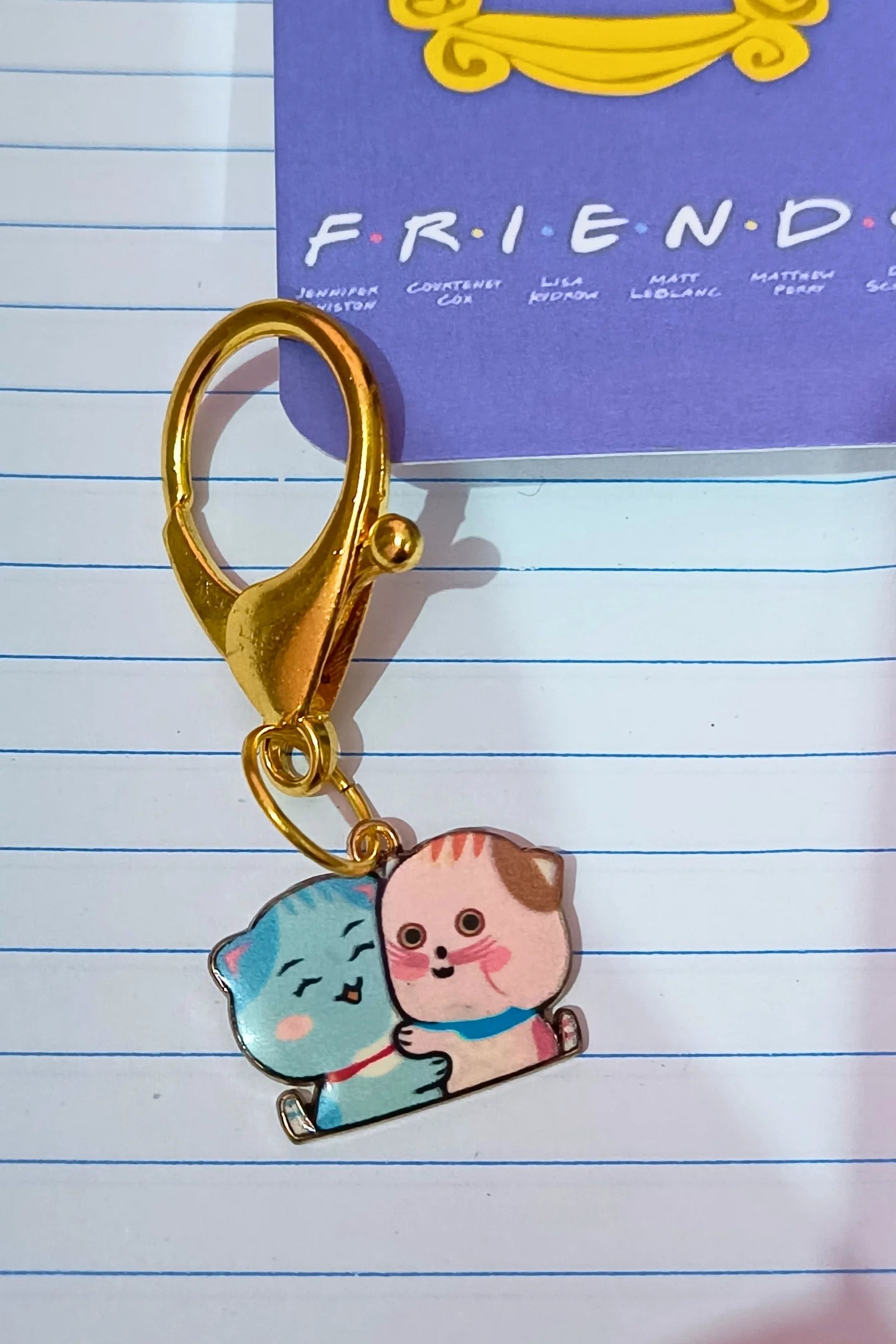 A couples keychain featuring two separate charms depicting cats hugging each other. The cats' colors may vary, including combinations of pink and blue.
