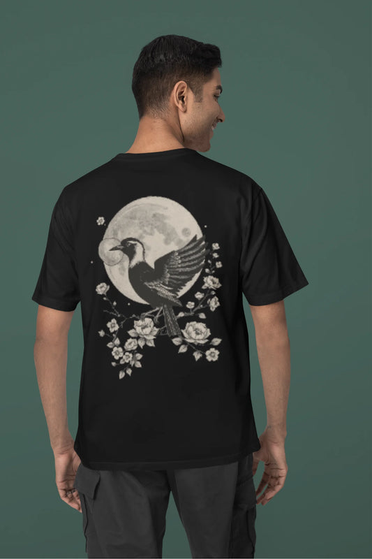 Back view of a male model wearing a black oversized tee with a heron taking off under the moonlight.