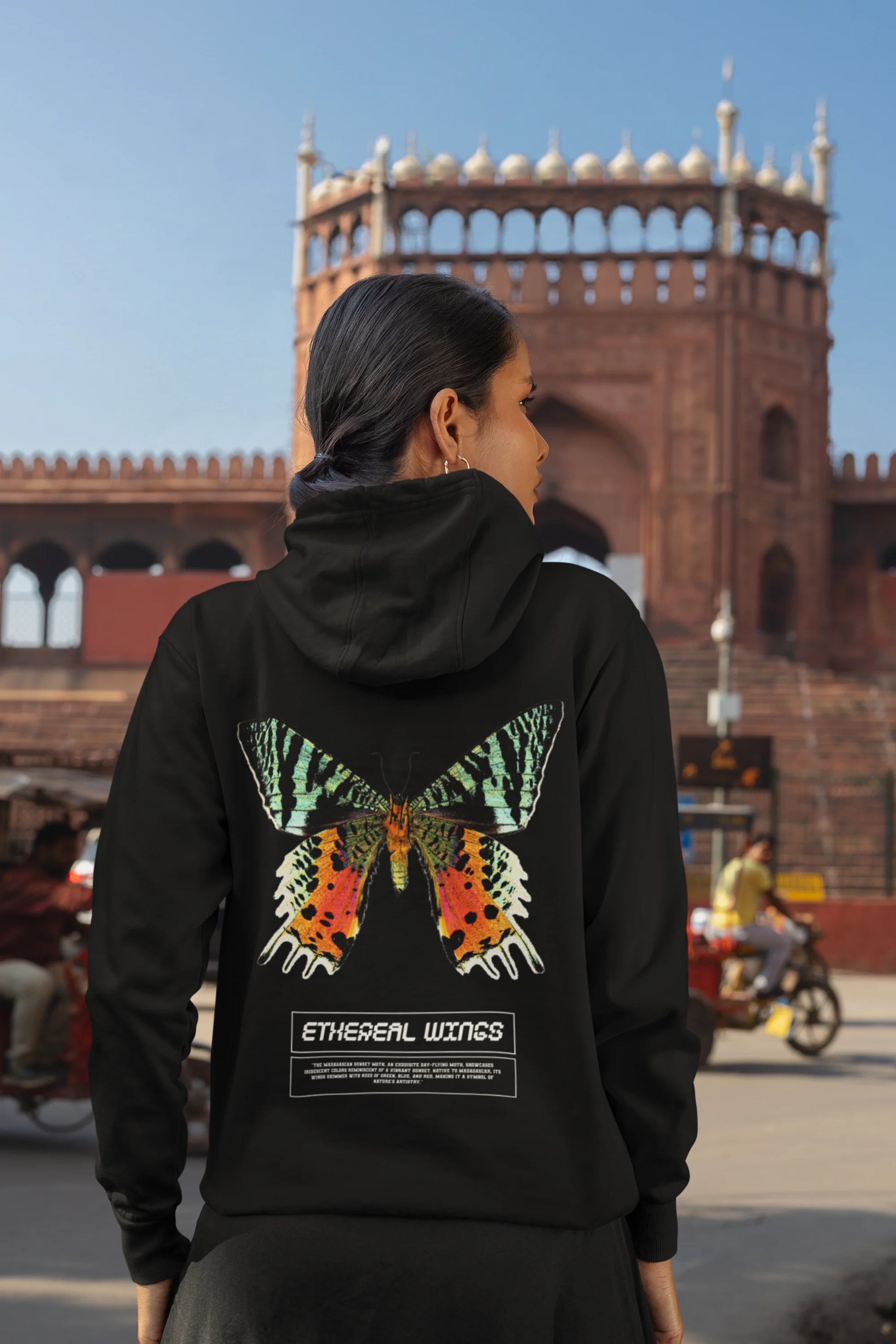 Back view of a female model wearing a black hoodie with a glowing butterfly design, symbolizing the ethereal beauty of nature.