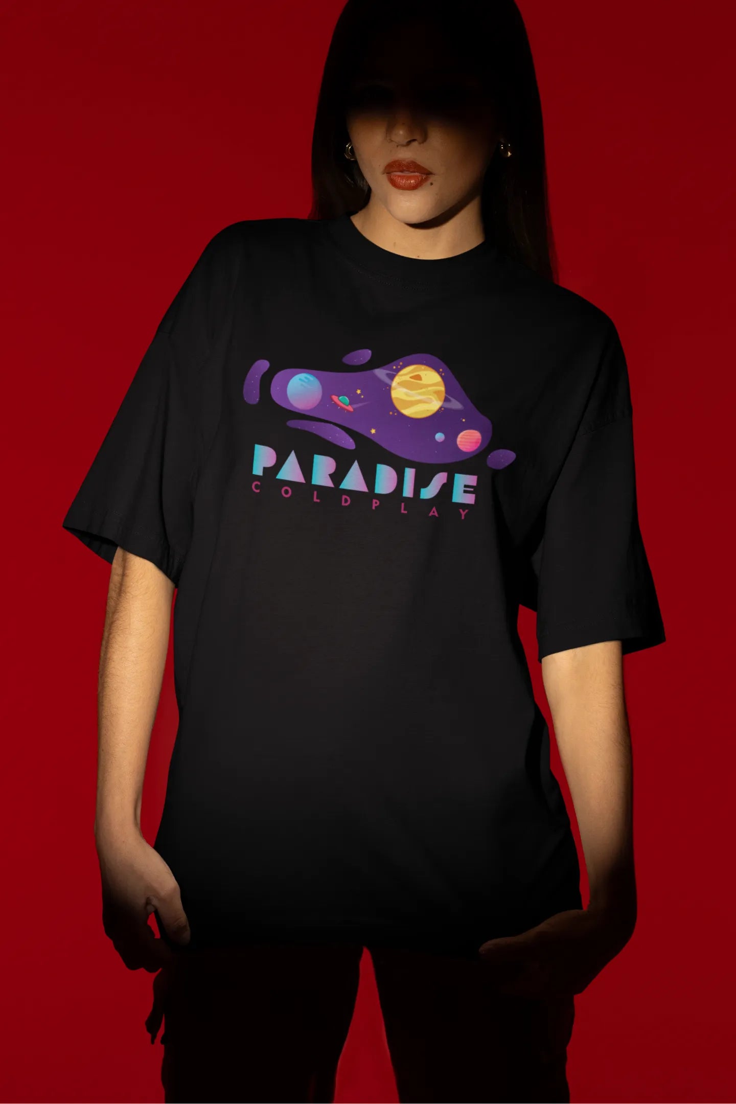 First front view of a female model wearing an black oversized t-shirt with the "Paradise" album artwork by Coldplay.
