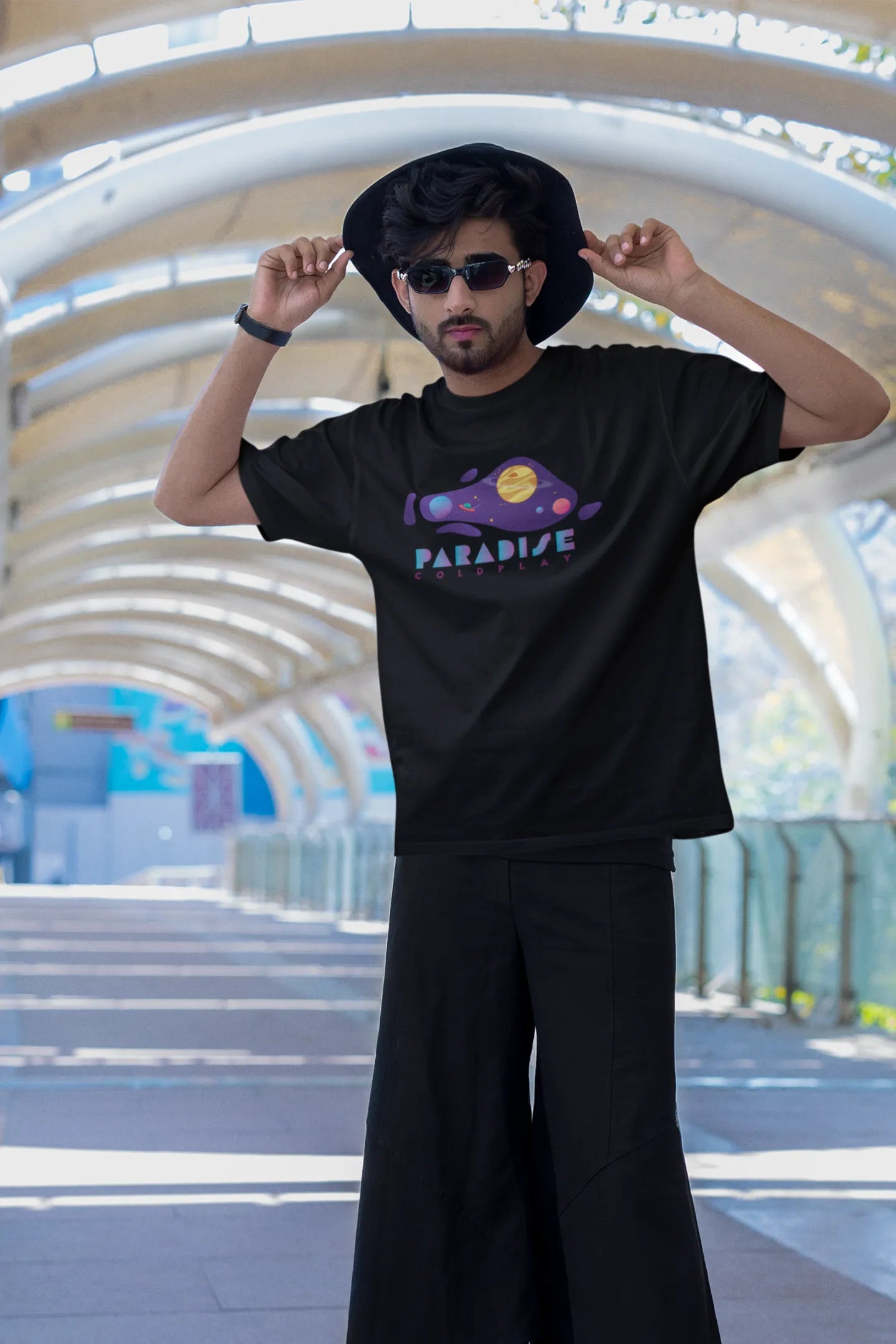First front view of a male model wearing an black oversized t-shirt with the "Paradise" album artwork by Coldplay.

