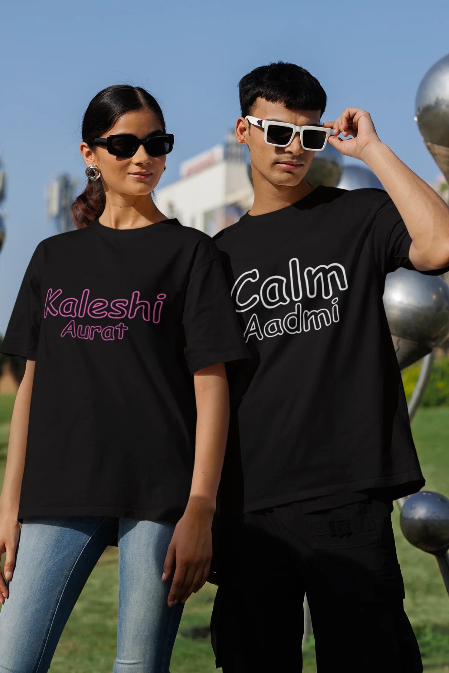 First front view of a couple wearing matching black oversize tees, one with "Calm one" and the other with "Chaotic one" printed on them in Hindi.