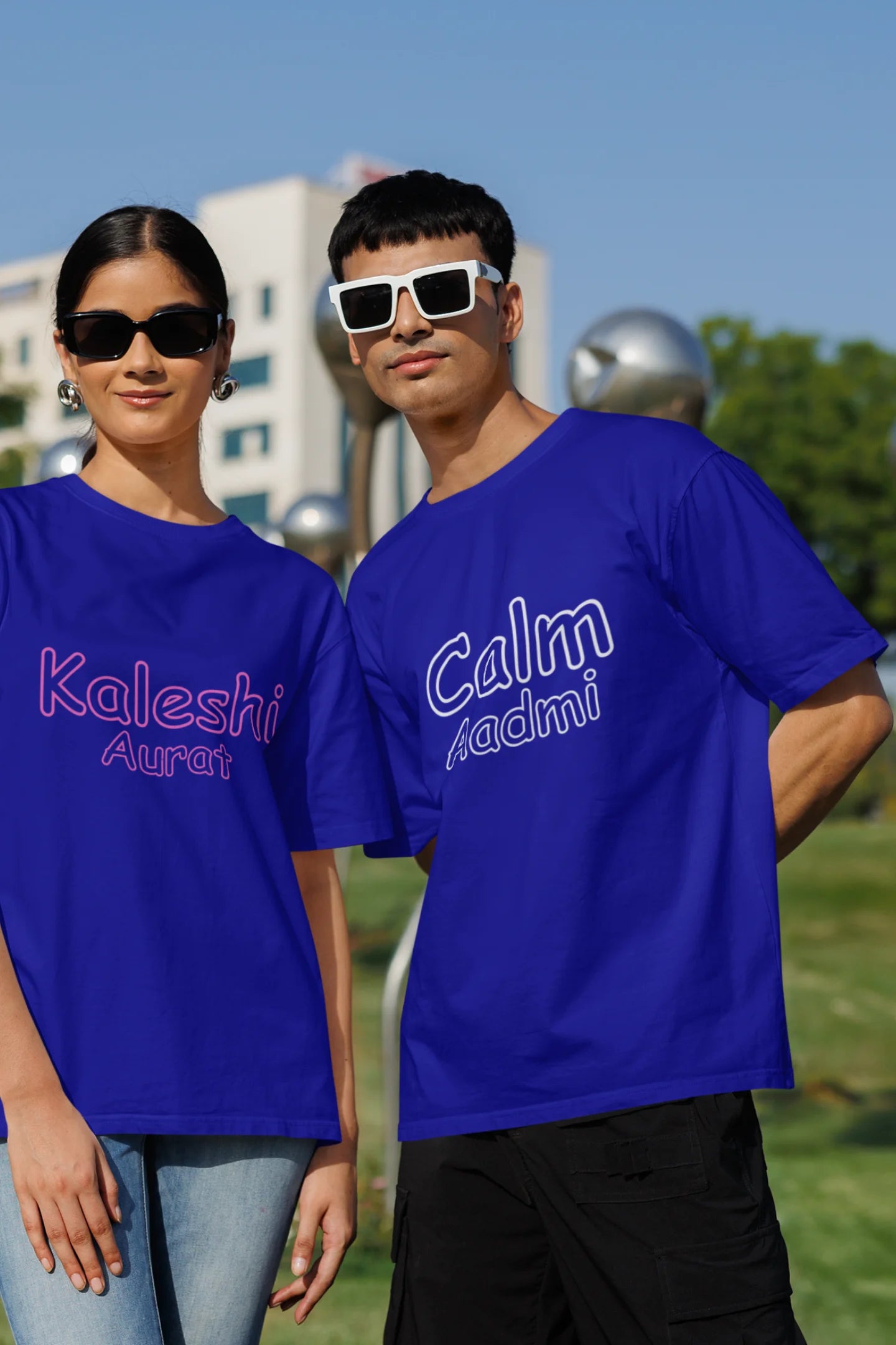 First front view of a couple wearing matching royal blue oversize tees, one with "Calm one" and the other with "Chaotic one" printed on them in Hindi.