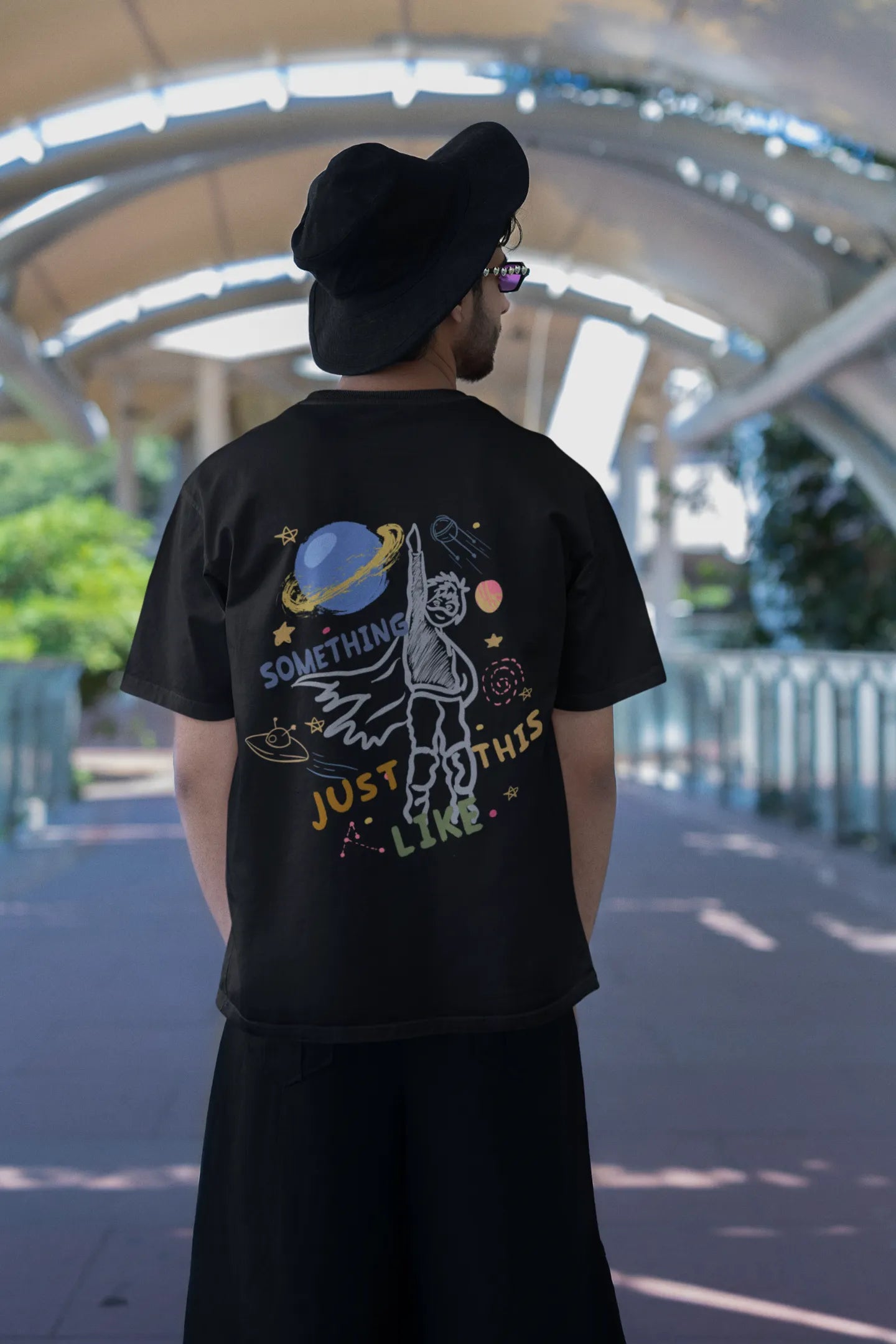 Back view of a male model wearing an black oversized t-shirt with a design inspired by the "Something Just Like This" music video, featuring the word "Superheroes".