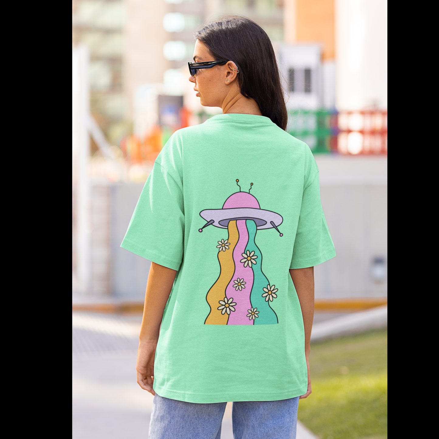 Back view of a female model wearing a mint green oversized t-shirt featuring a fun "Space Wreck" design with elements of spaceships, UFOs, and a hint of extraterrestrial life.