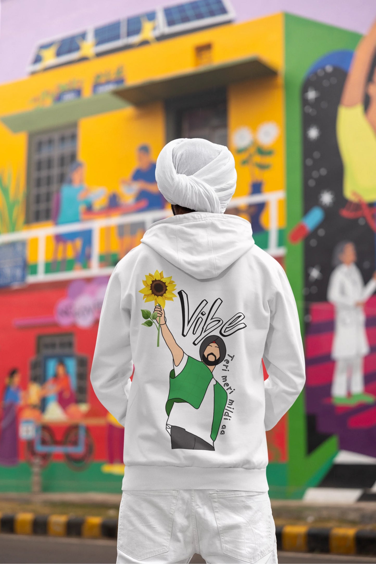 Back view of a male model wearing a comfortable white hoodie featuring the phrase "Vibe Teri Meri" in a modern font on a portrait of Diljit Singh holding up a sunflower, perfect for expressing your unique style and feeling the rhythm.