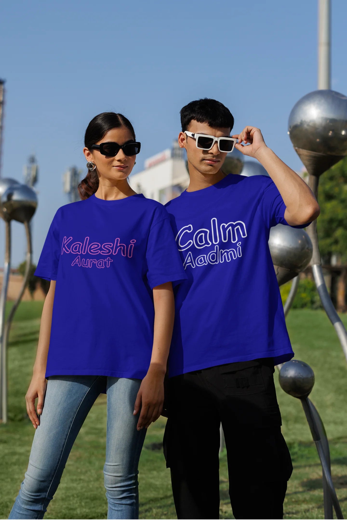 Second front view of a couple wearing matching royal blue oversize tees, one with "Calm one" and the other with "Chaotic one" printed on them in Hindi.