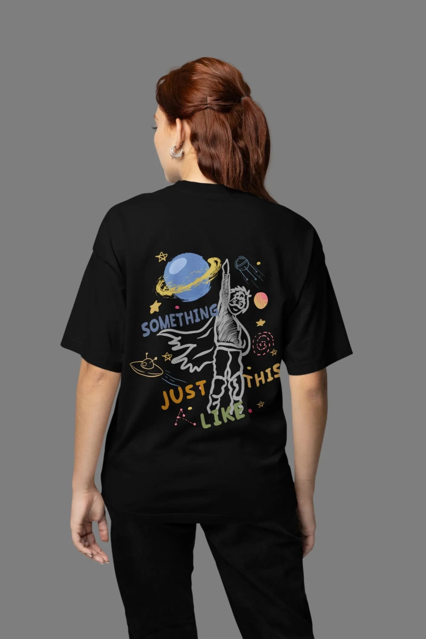 Back view of a female model wearing an black oversized t-shirt with a design inspired by the "Something Just Like This" music video, featuring the word "Superheroes".