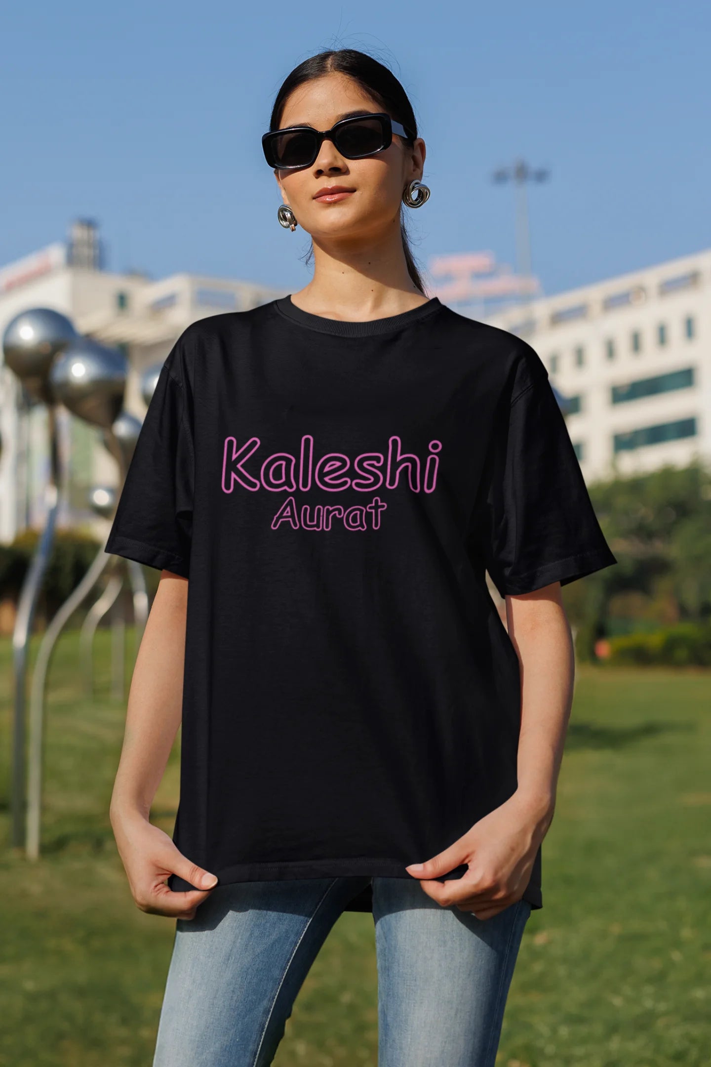 Front view of a the woman in the couple wearing matching black oversize tees, one with "Calm one" and the other with "Chaotic one" printed on them in Hindi.
