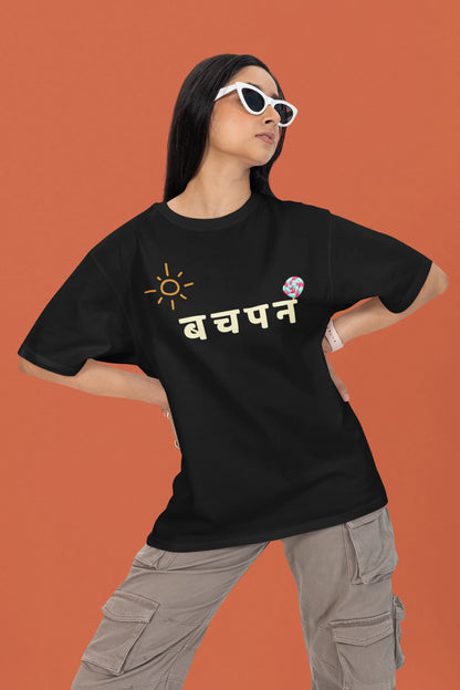 First front view of a female model wearing a black oversized t-shirt with a design representing "Bachpan" (childhood) and the concept of "Khatta Mitha" (sweet and sour).