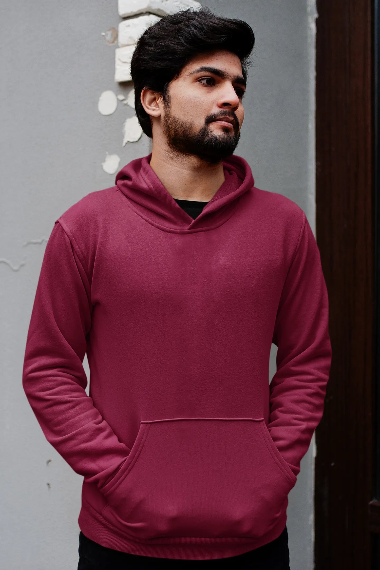First front view of a male model wearing a maroon hoodie with a design of a wildcat sitting on ocean waves.