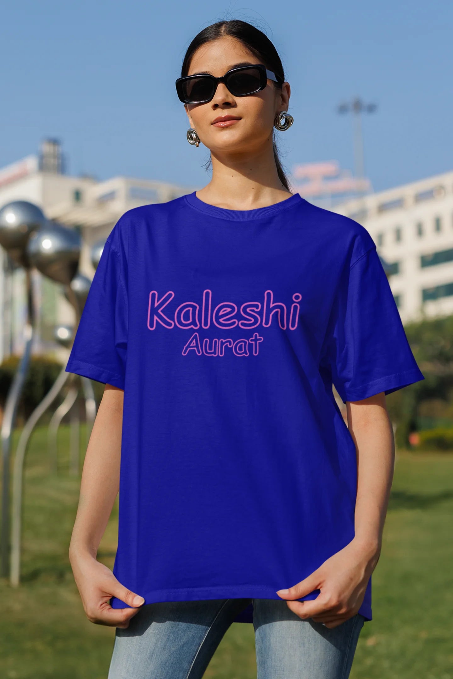 Front view of woman of the couple wearing matching royal blue oversize tees, one with "Calm one" and the other with "Chaotic one" printed on them in Hindi.