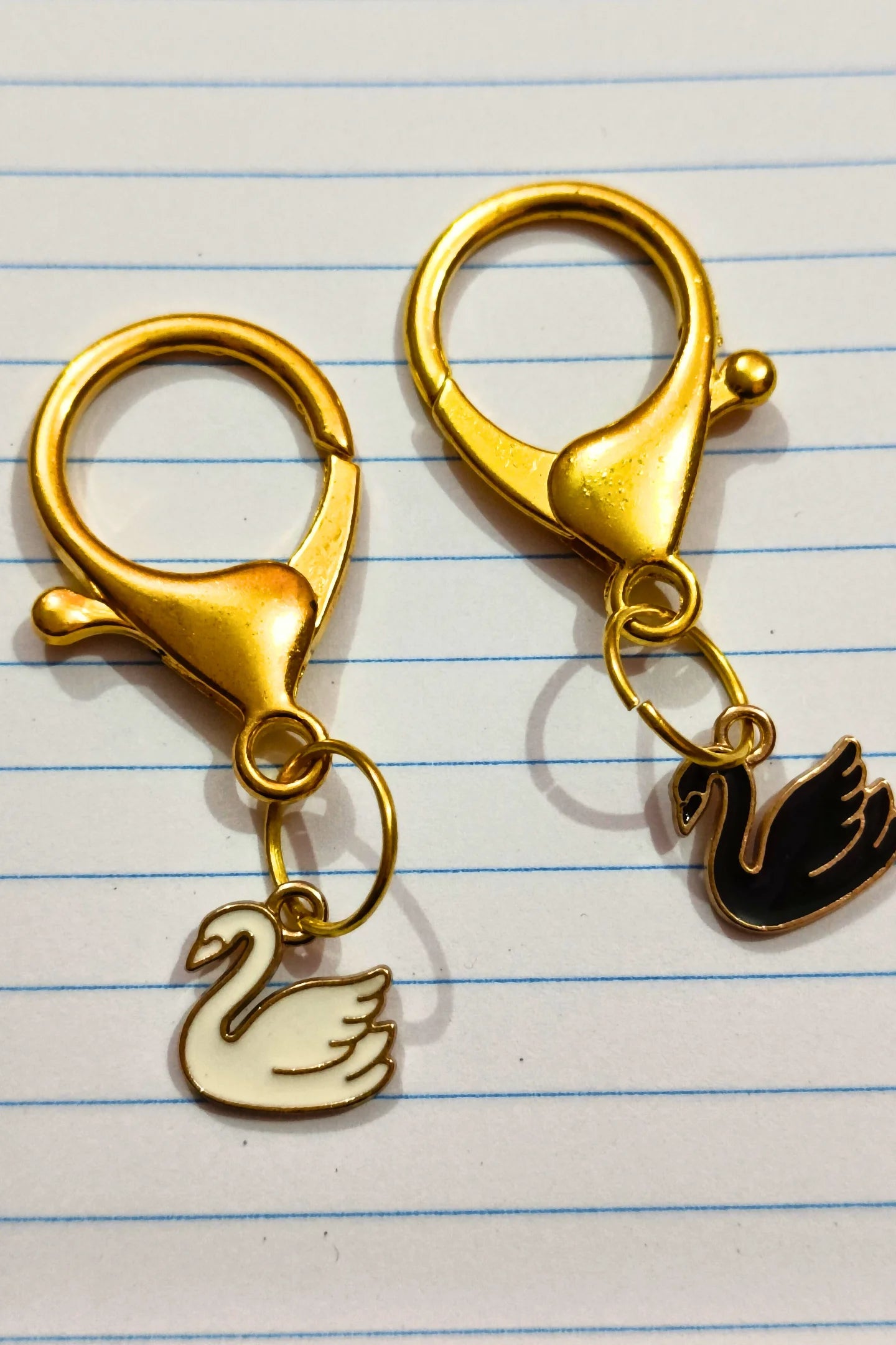 A view of a couples keychain featuring two separate charms: one of a black swan and one of a white swan.