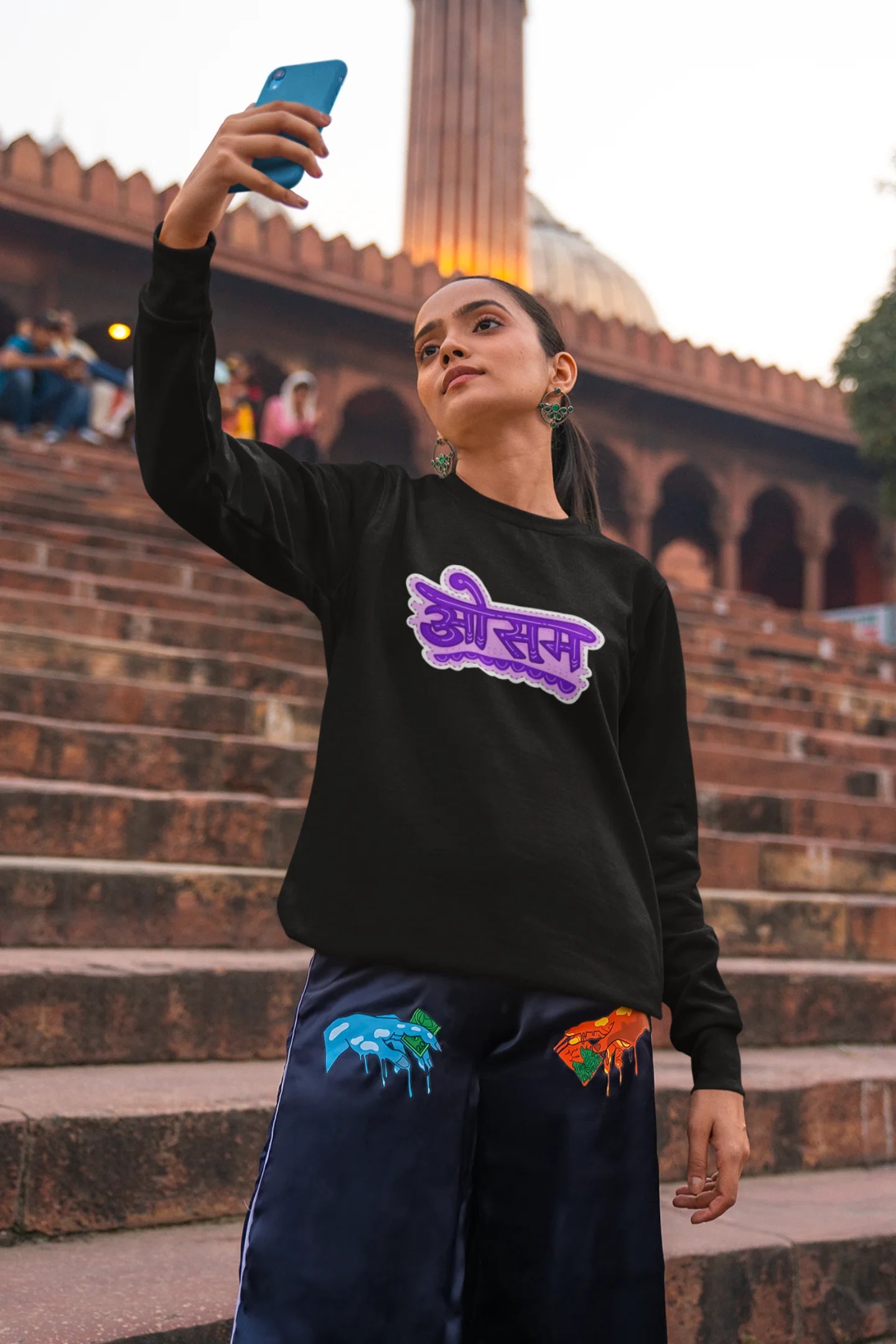 6th front view of a female model wearing a black colored oversized graphic t-shirt featuring the word "awesome" in a Hindi script.