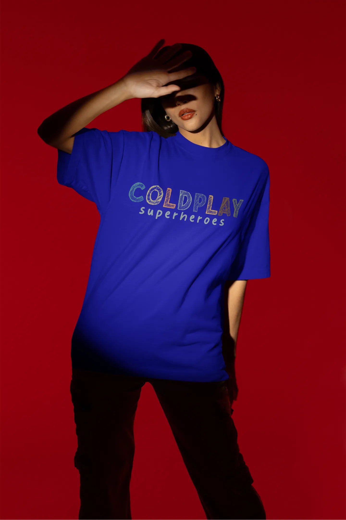 Fourth view of a female model wearing an royal blue oversized t-shirt with a design inspired by the "Something Just Like This" music video, featuring the word "Superheroes".