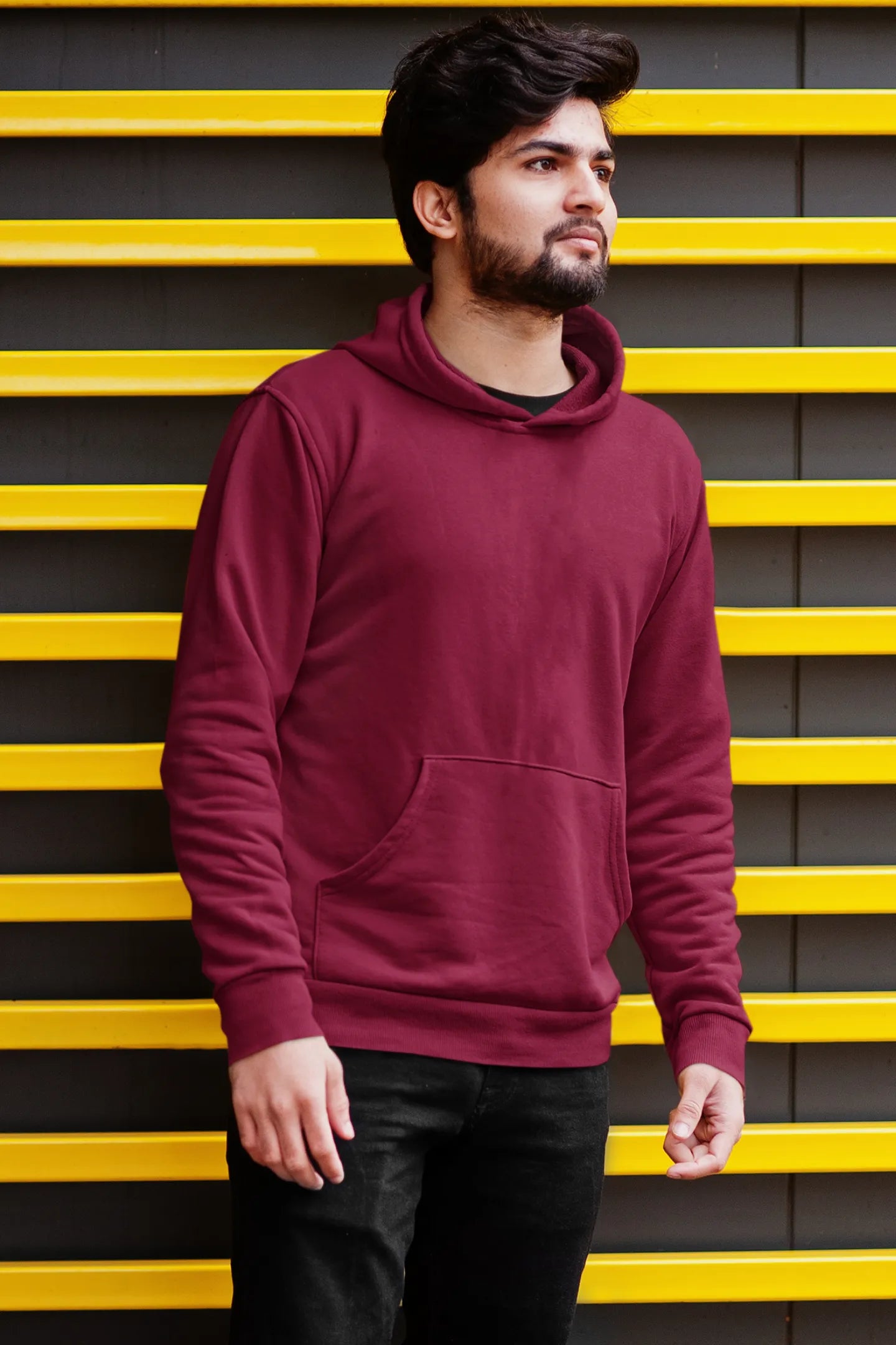 Third front view of a male model wearing a maroon hoodie with a design of a wildcat sitting on ocean waves.
