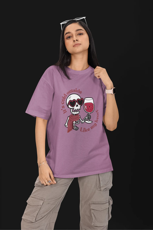 First front image of a female model wearing a dirty purple oversized t-shirt with the text "Cold Outside Like My Heart" and a design of a skeleton drinking champagne.