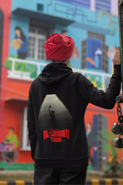Back view of a female model wearing a black hoodie with a portrait of Diljit Dosanjh on stage, illuminated by a spotlight.