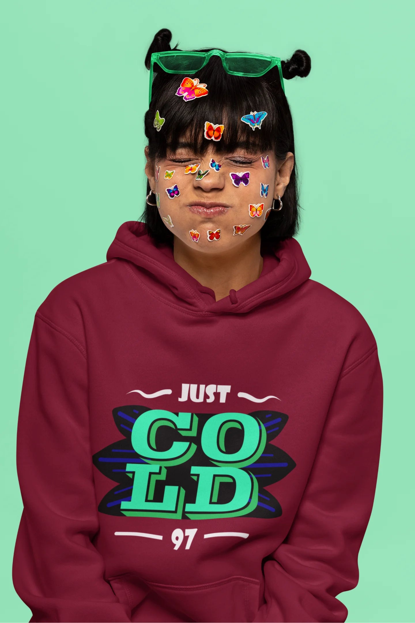 6th front view of a female model wearing an maroon sweatshirt with the text "Just Cold" printed on it.