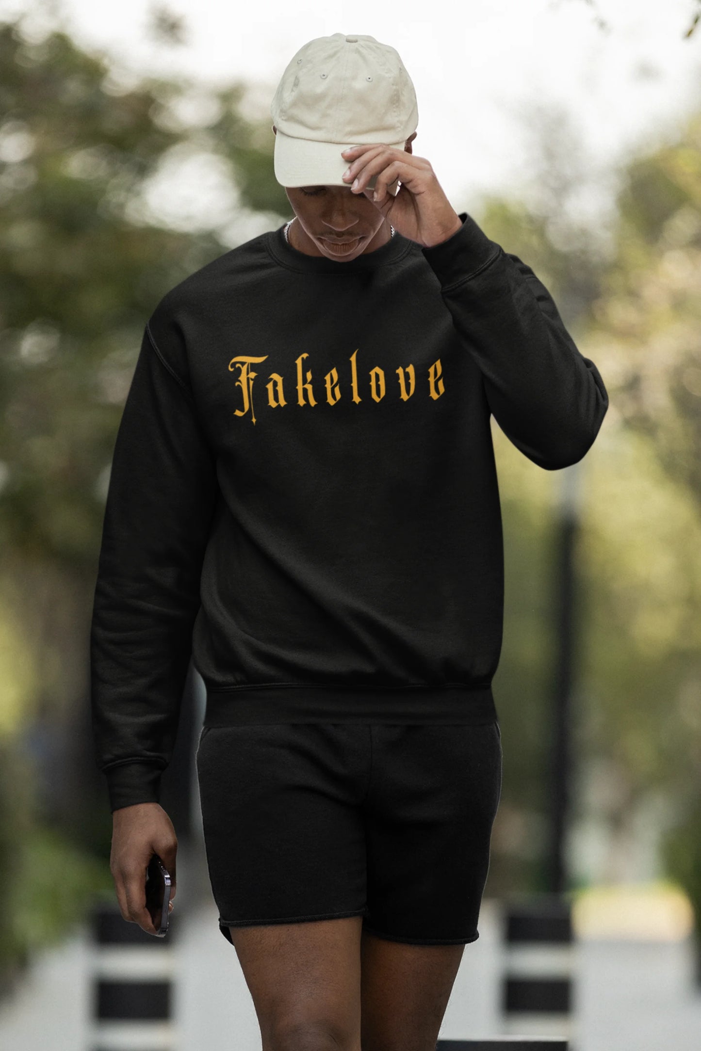 First front view of a male model wearing a black sweatshirt with a brutalist design featuring a fallen angel statue and the phrase "Fake Love".