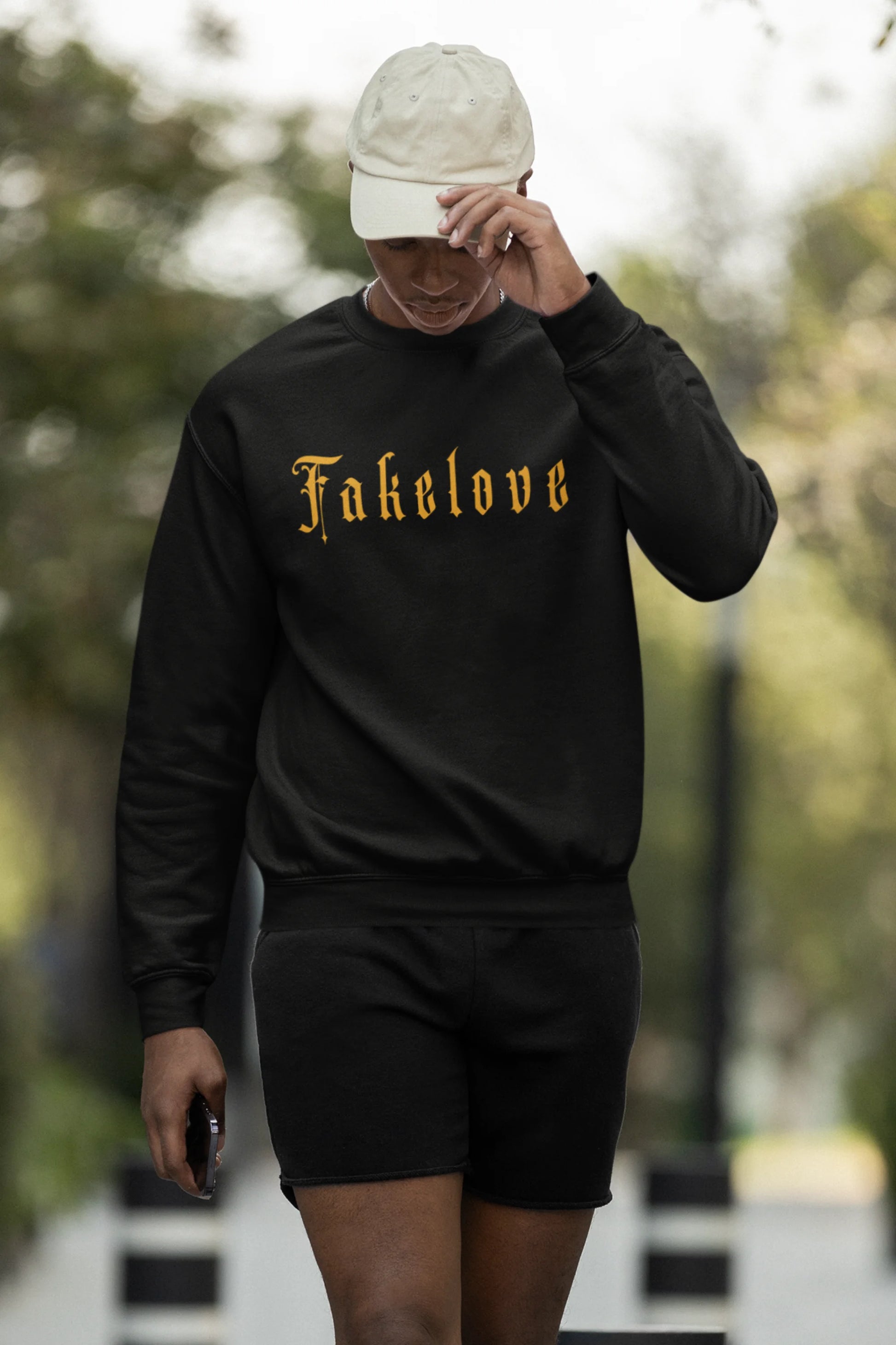First front view of a male model wearing a black sweatshirt with a brutalist design featuring a fallen angel statue and the phrase "Fake Love".