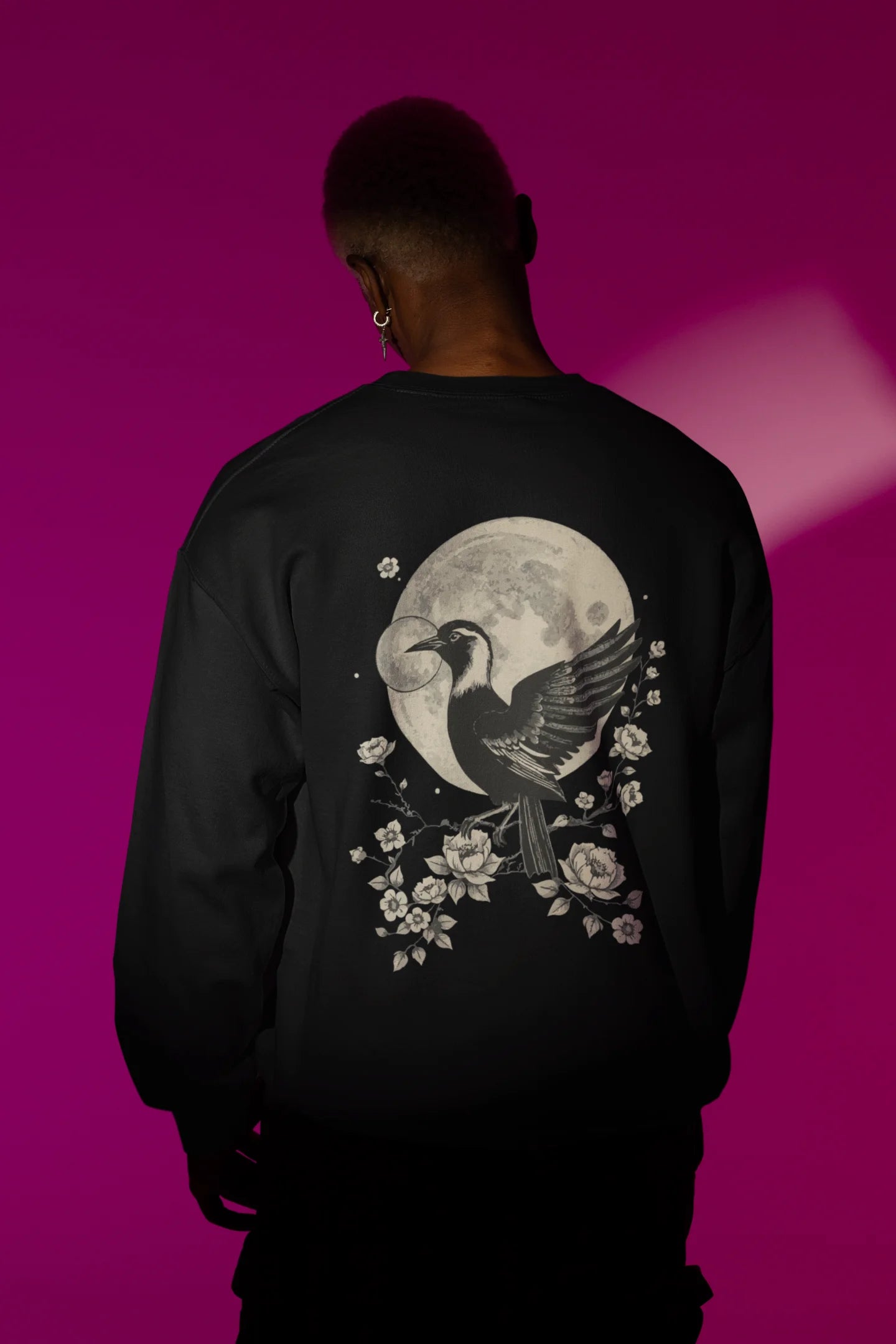 Back view of a male model wearing a black sweatshirt with a heron taking off under the moonlight.