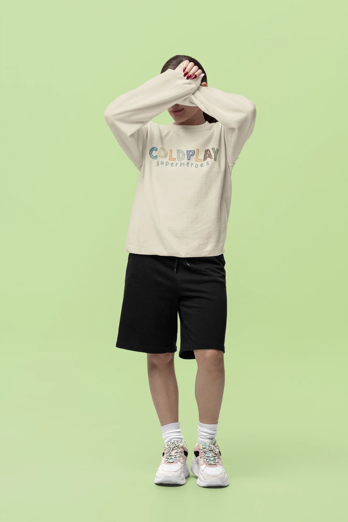 Fourth front view of a female model wearing an cream sweatshirt with a design inspired by the "Something Just Like This" music video, featuring the word "Superheroes".