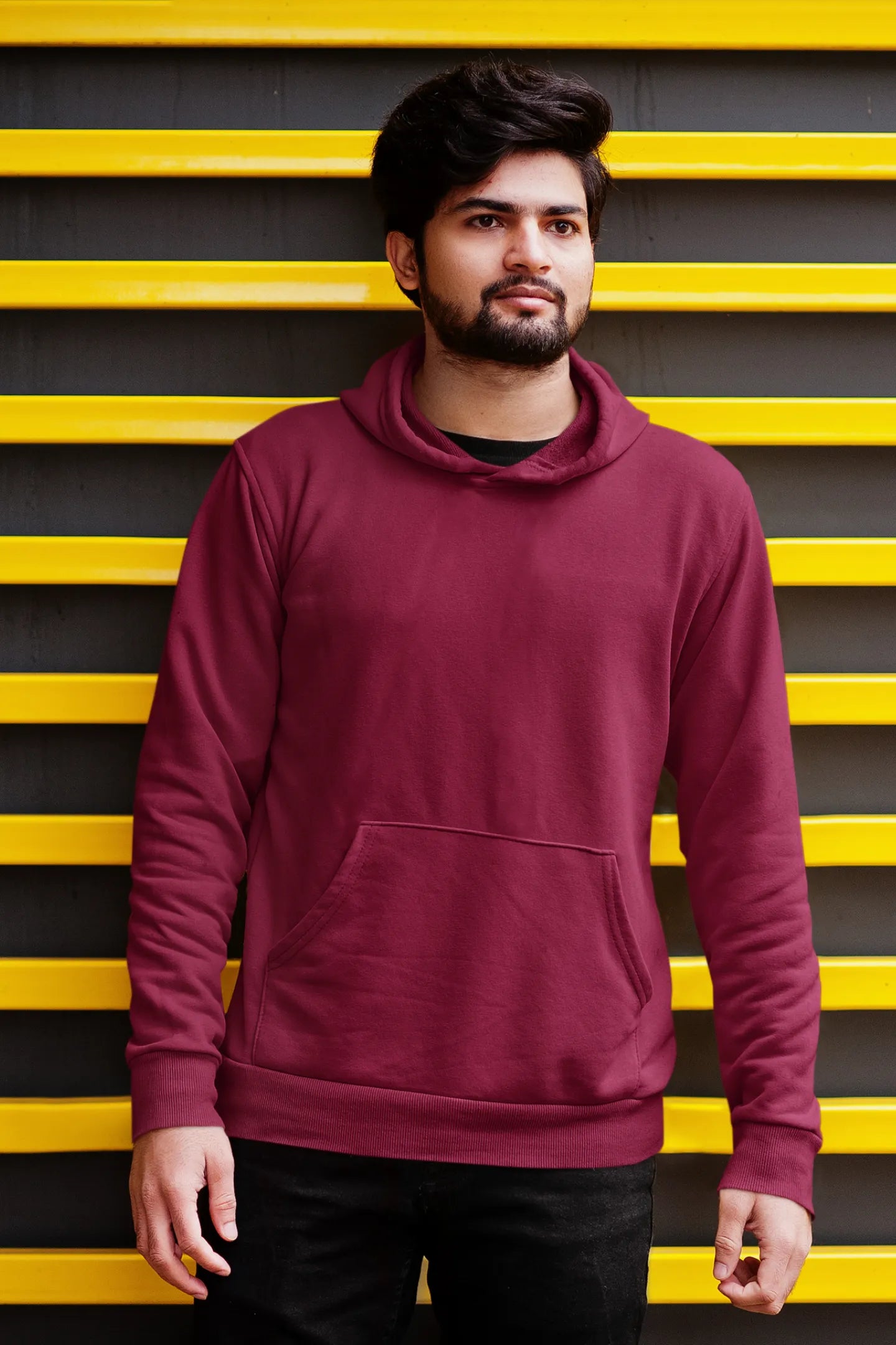 Second front view of a male model wearing a maroon hoodie with a design of a wildcat sitting on ocean waves.