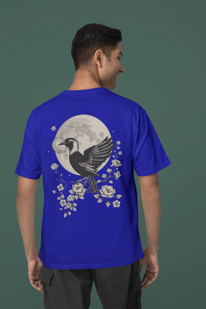 Back view of a male model wearing a royal blue oversized tee with a heron taking off under the moonlight.