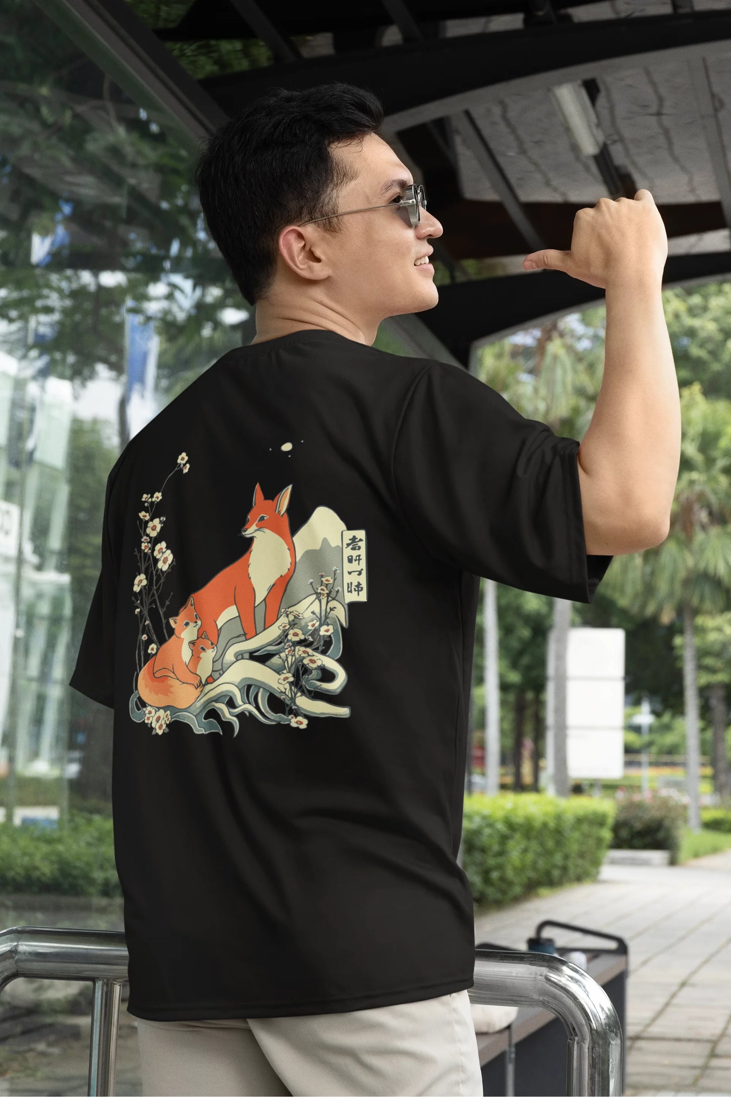 First back view of a male model wearing a black oversized tee with a design of a fox and its cub in a traditional Japanese landscape.