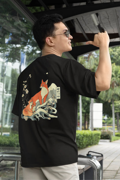First back view of a male model wearing a black oversized tee with a design of a fox and its cub in a traditional Japanese landscape.