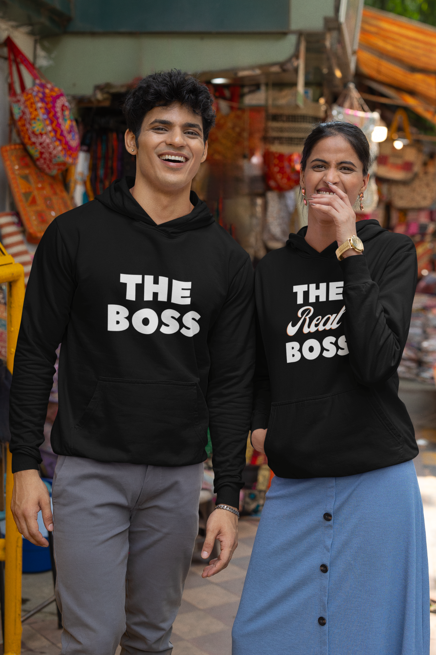A smiling couple wearing matching hoodies, one with "The Boss" and the other with "The Real Boss" printed on them.