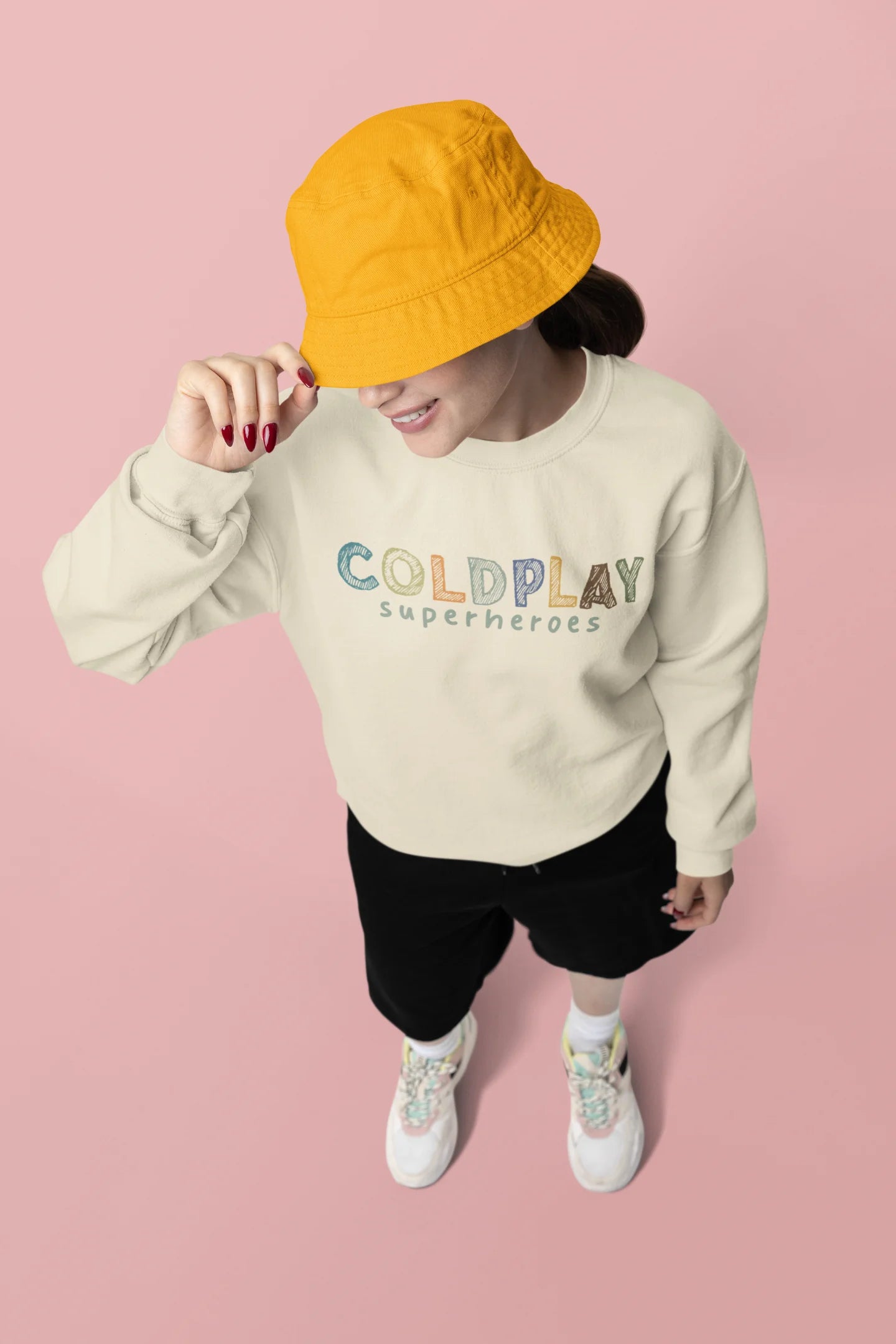Second front view of a female model wearing an cream sweatshirt with a design inspired by the "Something Just Like This" music video, featuring the word "Superheroes".