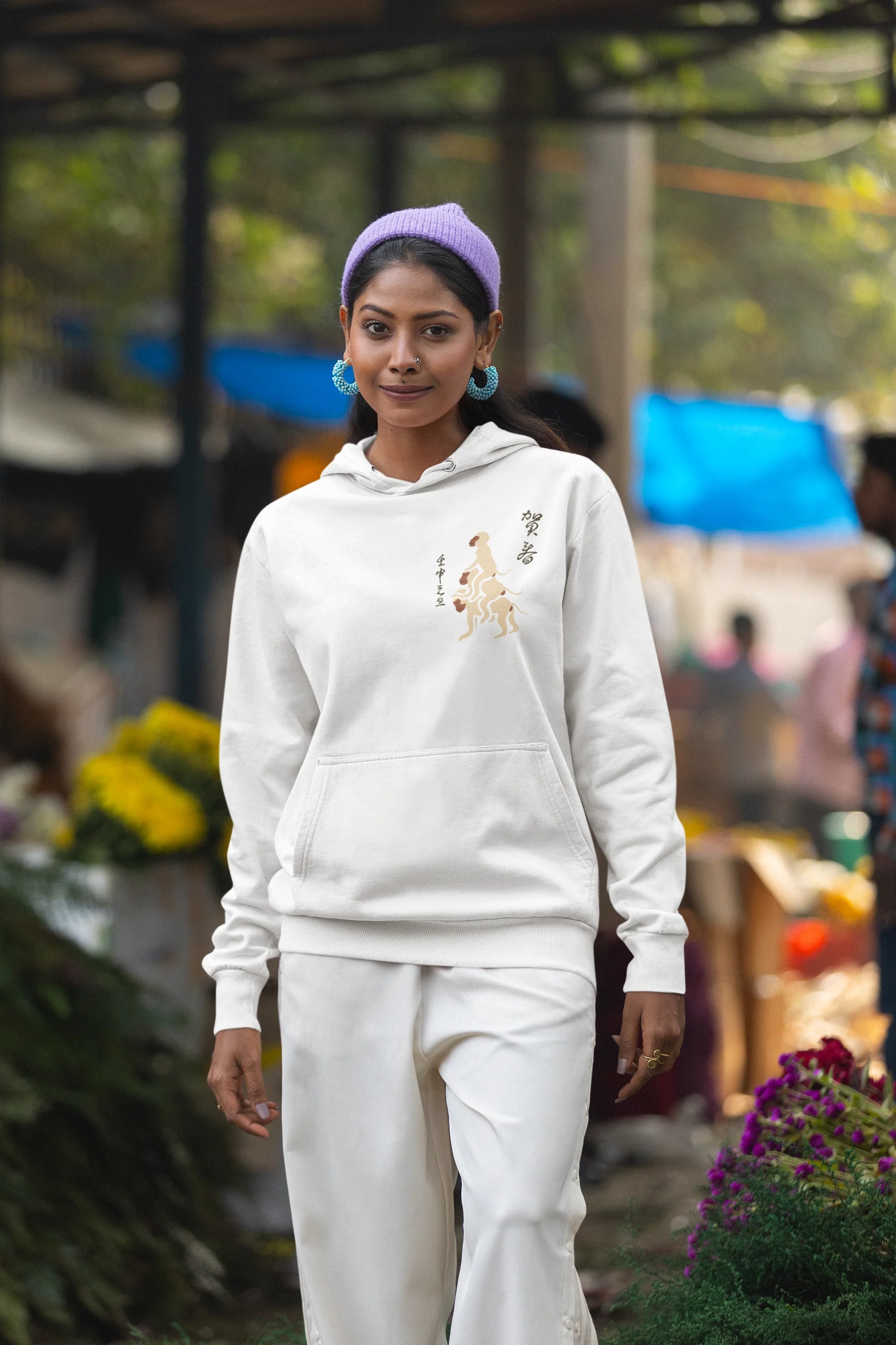 First front view of a female model wearing a white hoodie with a design of the three wise monkeys: "See no evil, hear no evil, speak no evil."