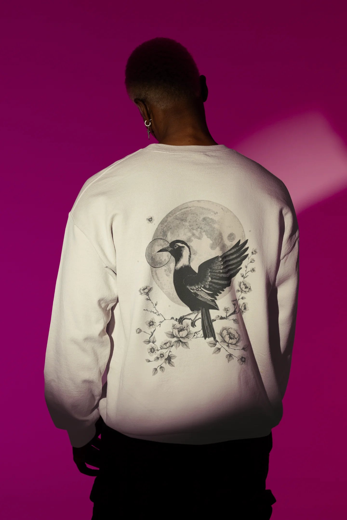 Back view of a male model wearing a cream sweatshirt with a heron taking off under the moonlight.