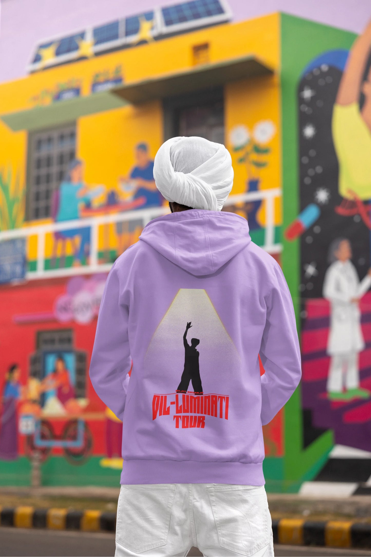 Back view of a male model wearing a dirty purple hoodie with a portrait of Diljit Dosanjh on stage, illuminated by a spotlight.