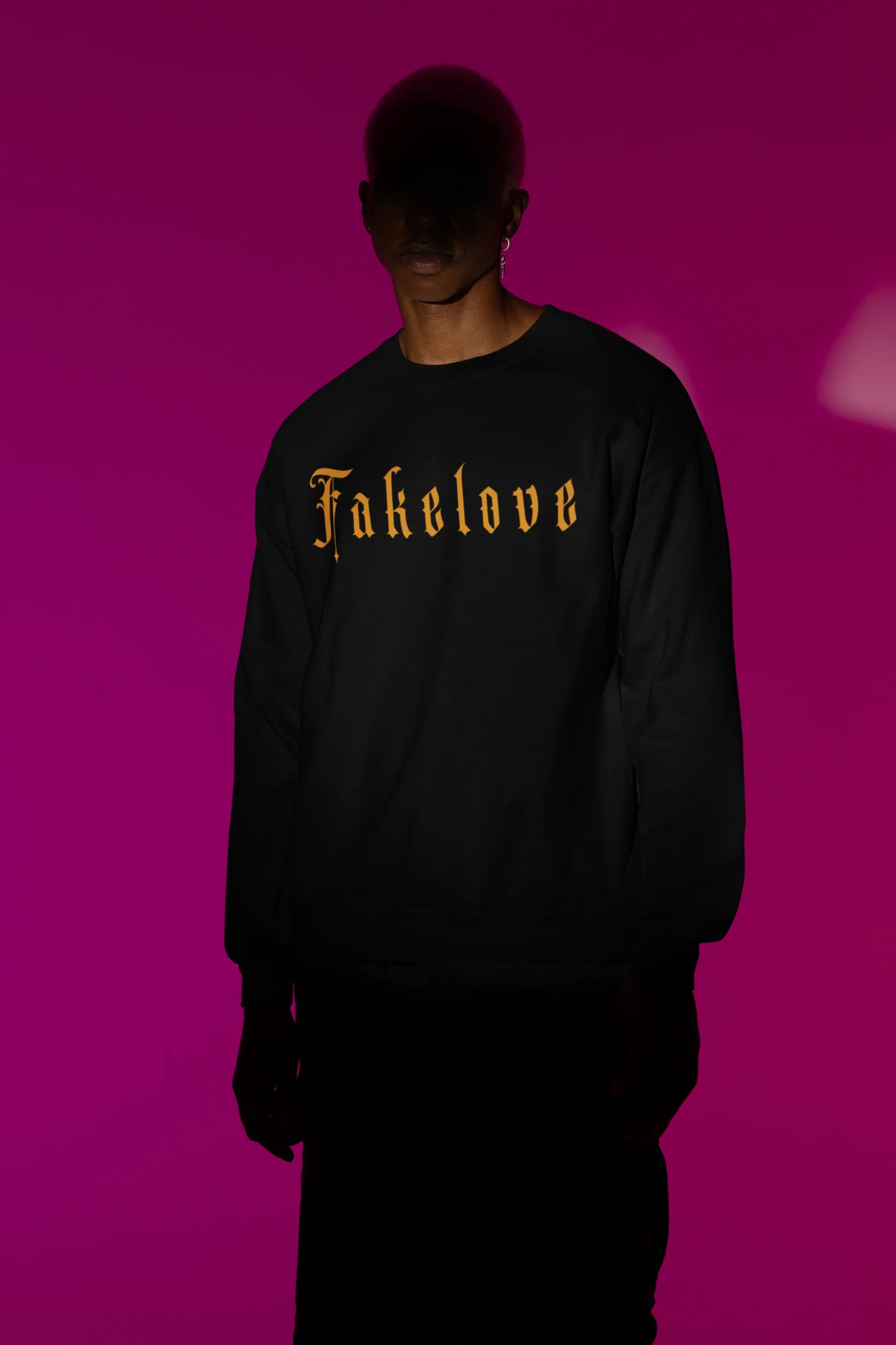 Second front view of a male model wearing a black sweatshirt with a brutalist design featuring a fallen angel statue and the phrase "Fake Love".