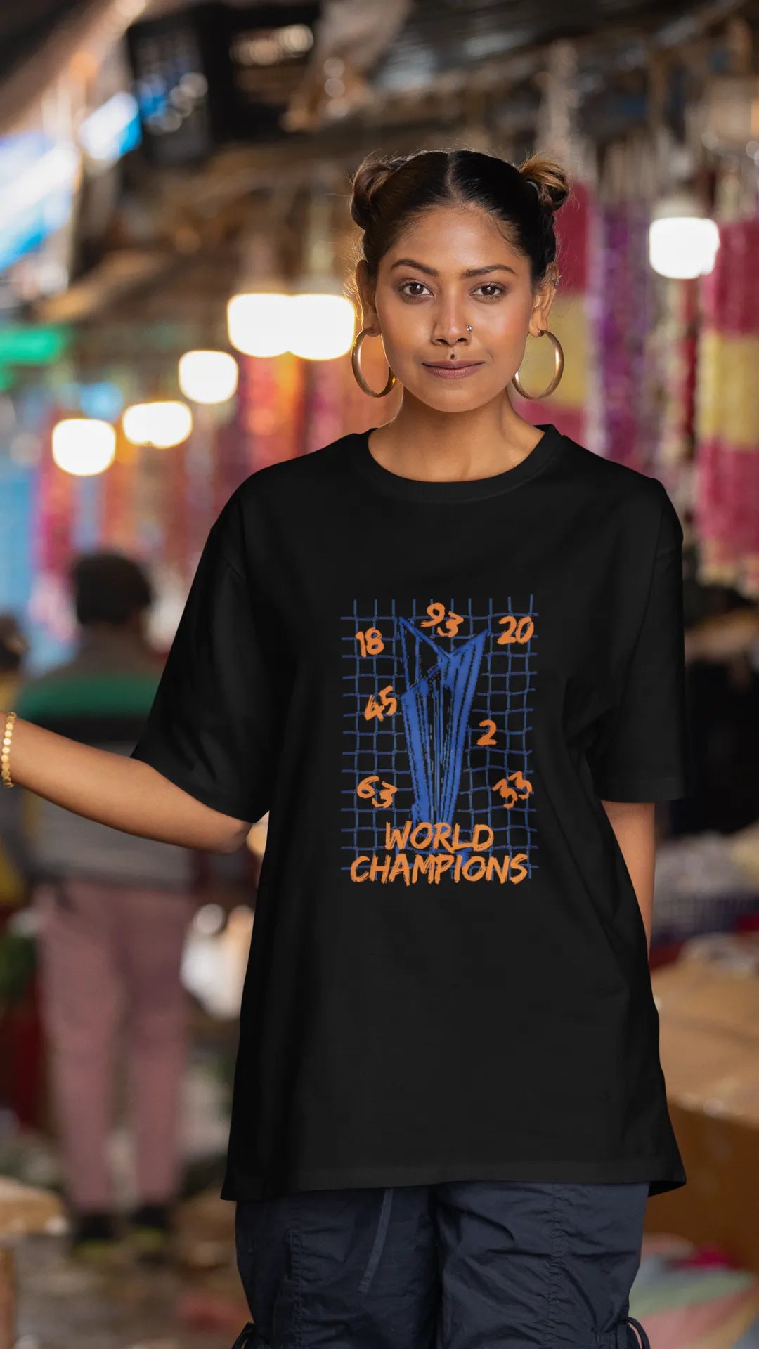 Second front image of female model wearing a black oversized t-shirt featuring the World Cup 2024 trophy with the text "World Champions" underneath. Ideal for Indian cricket fans celebrating their team's victory.