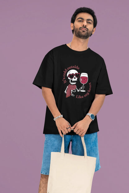 First front image of a male model wearing a black oversized t-shirt with the text "Cold Outside Like My Heart" and a design of a skeleton drinking champagne.