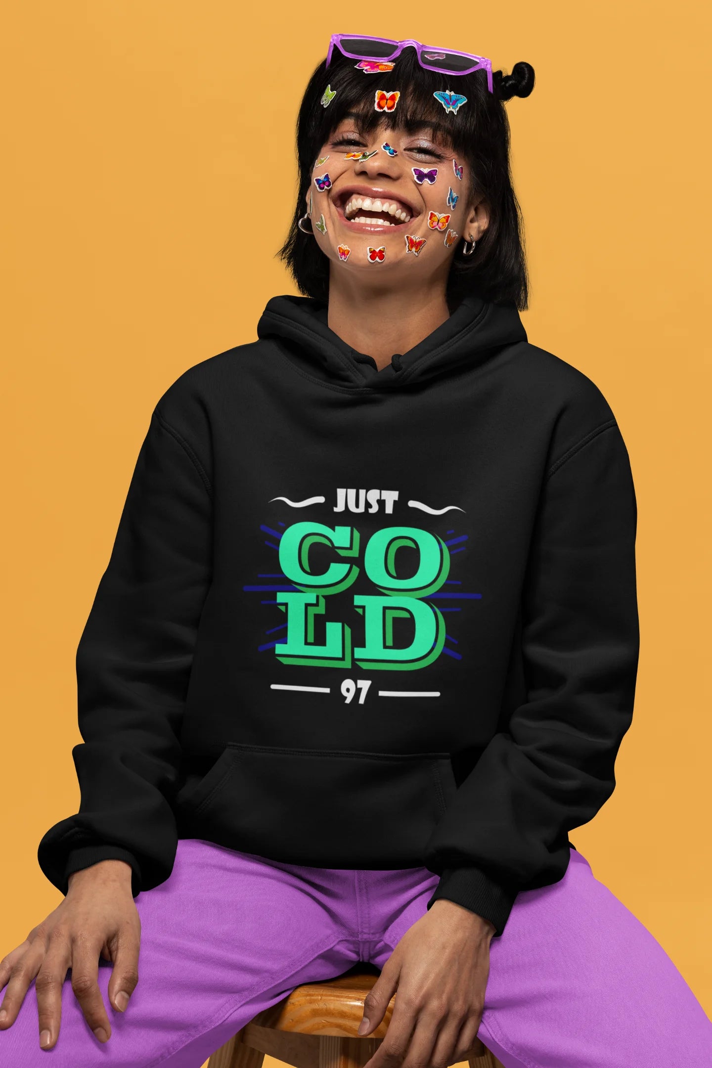 5th front view of a female model wearing an black sweatshirt with the text "Just Cold" printed on it.