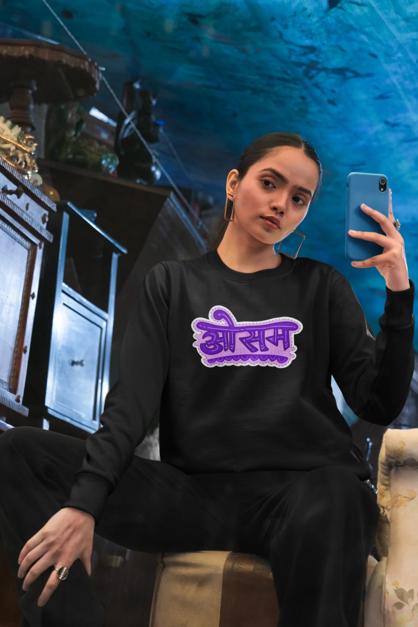 First front view of a female model wearing a black colored oversized graphic t-shirt featuring the word "awesome" in a Hindi script.