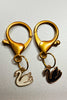 A couples keychain featuring two separate charms: one of a black swan and one of a white swan.