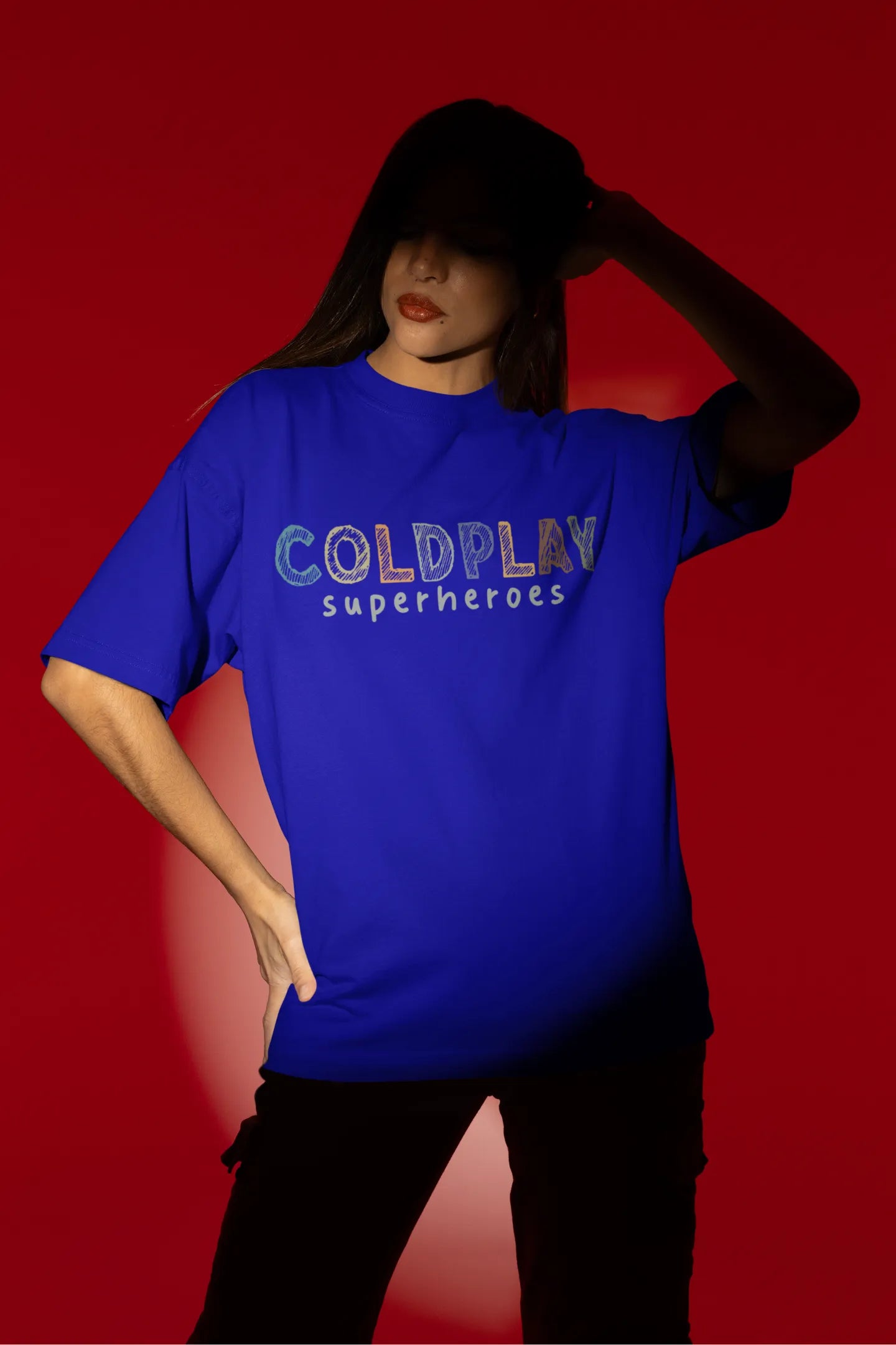 Third view of a female model wearing an royal blue oversized t-shirt with a design inspired by the "Something Just Like This" music video, featuring the word "Superheroes".