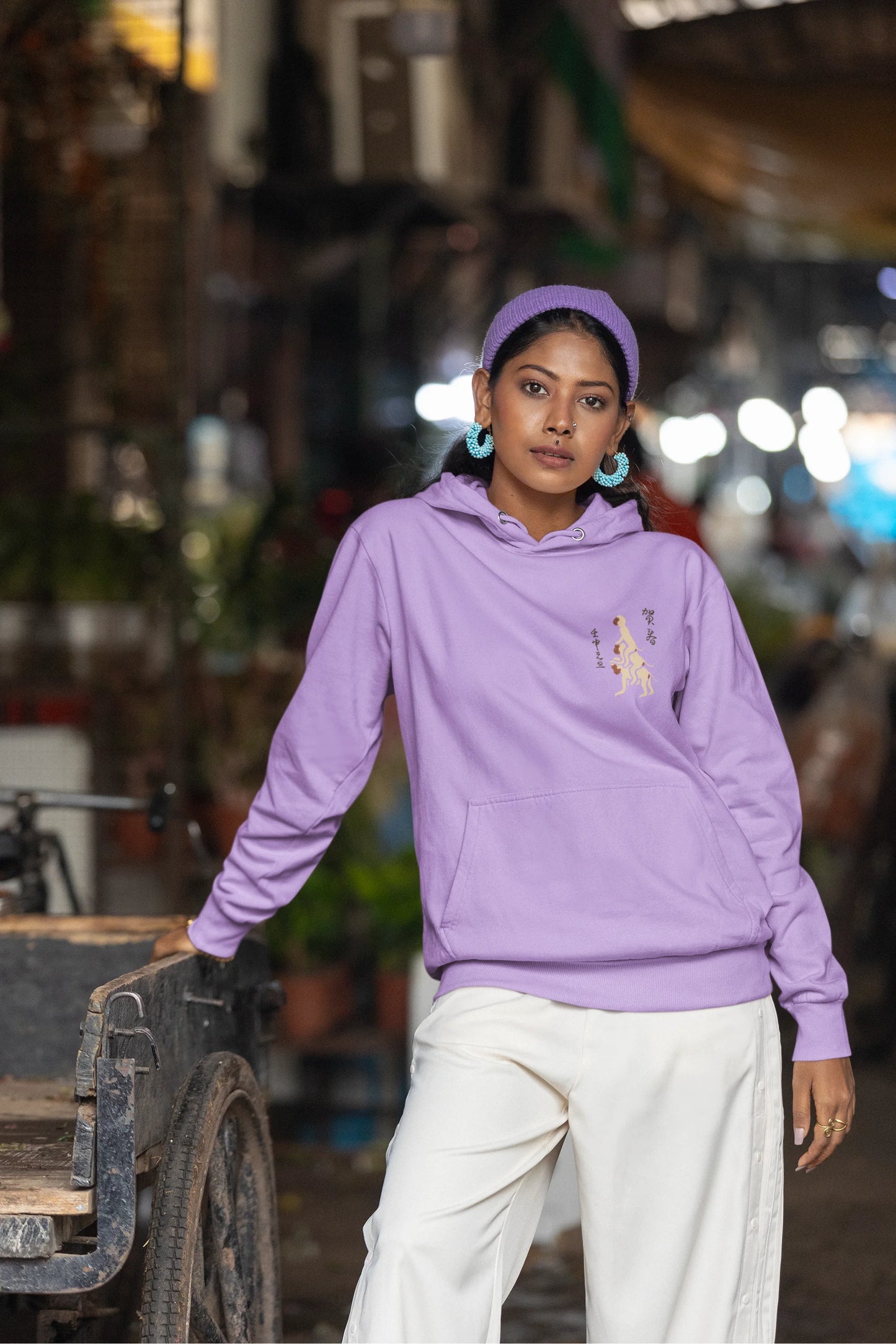 Third front view of a female model wearing a lavender hoodie with a design of the three wise monkeys: "See no evil, hear no evil, speak no evil."