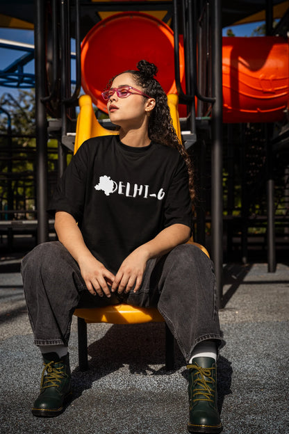 Side view of a female model wearing a black oversized t-shirt featuring a design incorporating the Red Fort and elements representing the city of Delhi, inspired by the Hindi film Delhi 6.
