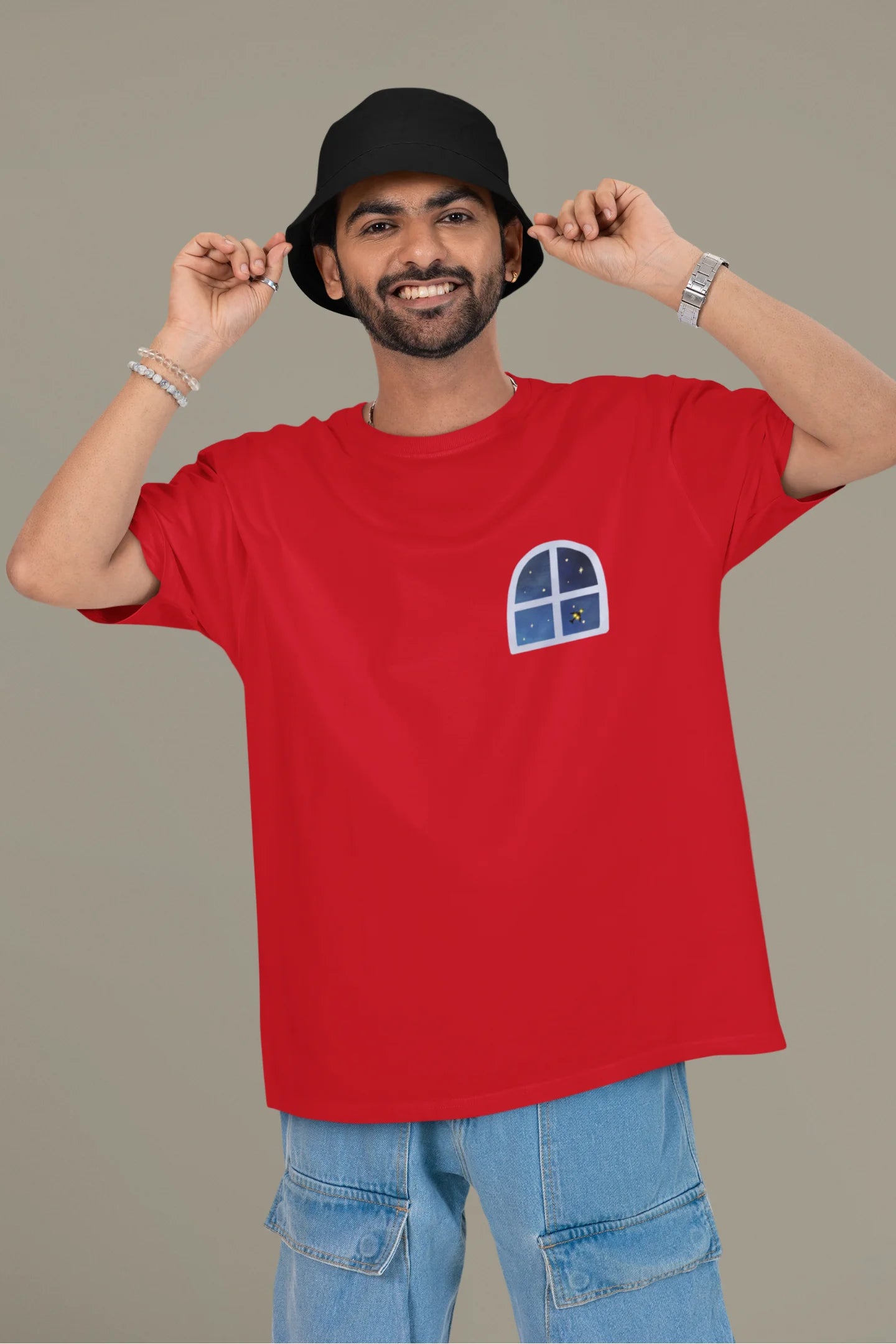 First front view of a male model wearing an oversized t-shirt featuring an illustration called Mithi Neend of children lying or sitting on a rooftop, looking up at a starry night sky.