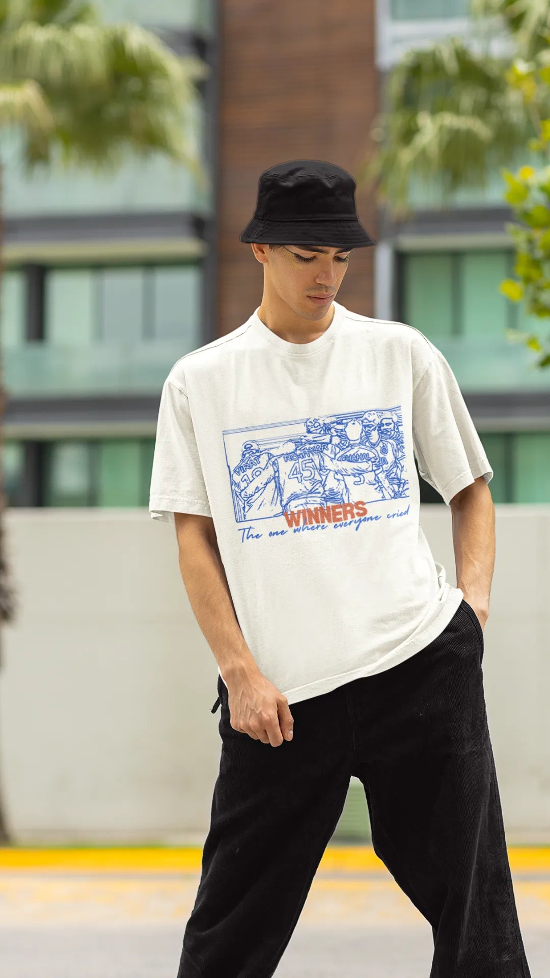 Front view of a male model wearing an of-white oversized t-shirt featuring a design of the Indian cricket team in a celebratory huddle with the text "Winners" above them. Ideal for Indian cricket fans commemorating their team's World Cup victory.