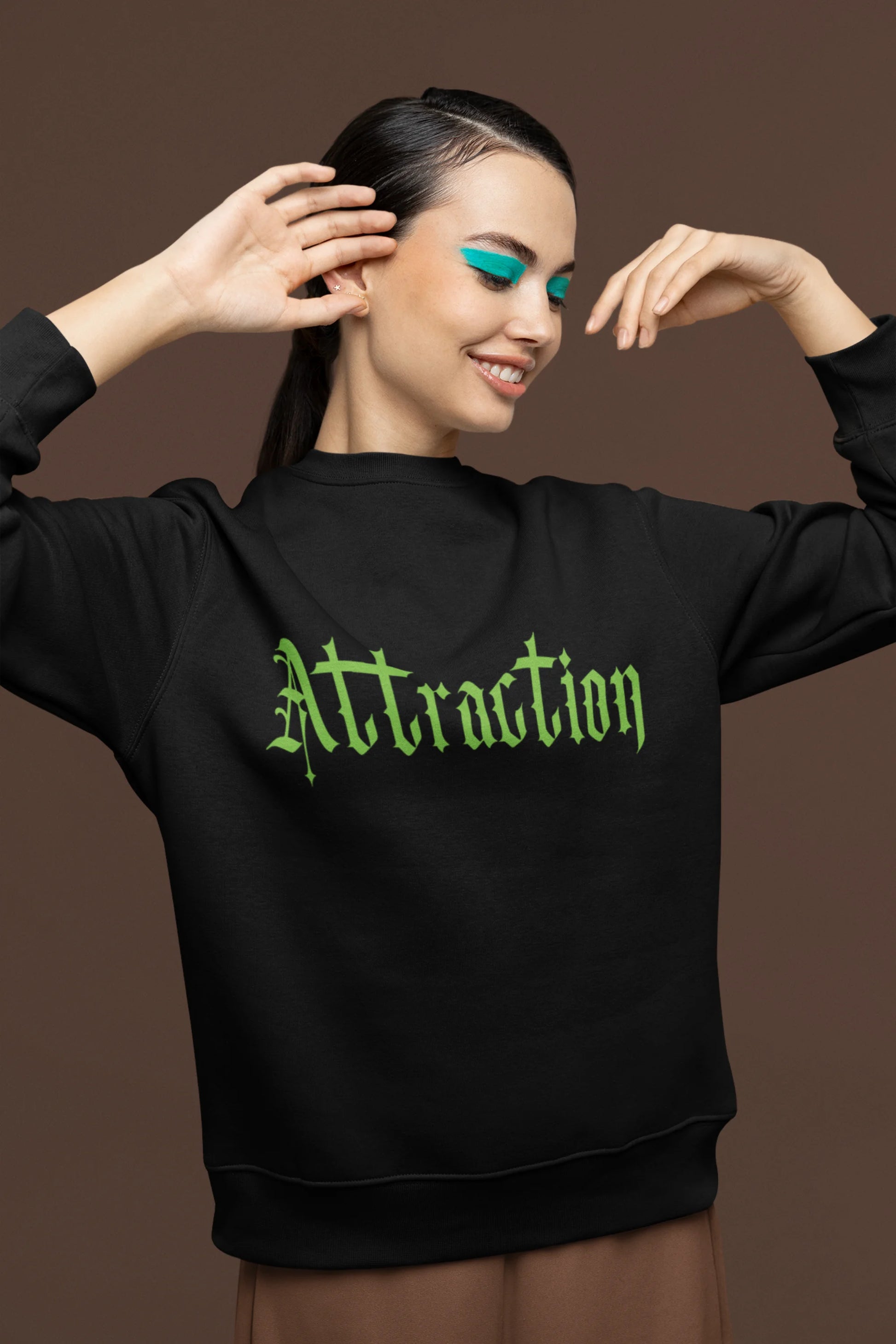 First front view of a female model wearing a black sweatshirt with a brutalist design featuring two statues kissing and the word "Attraction".