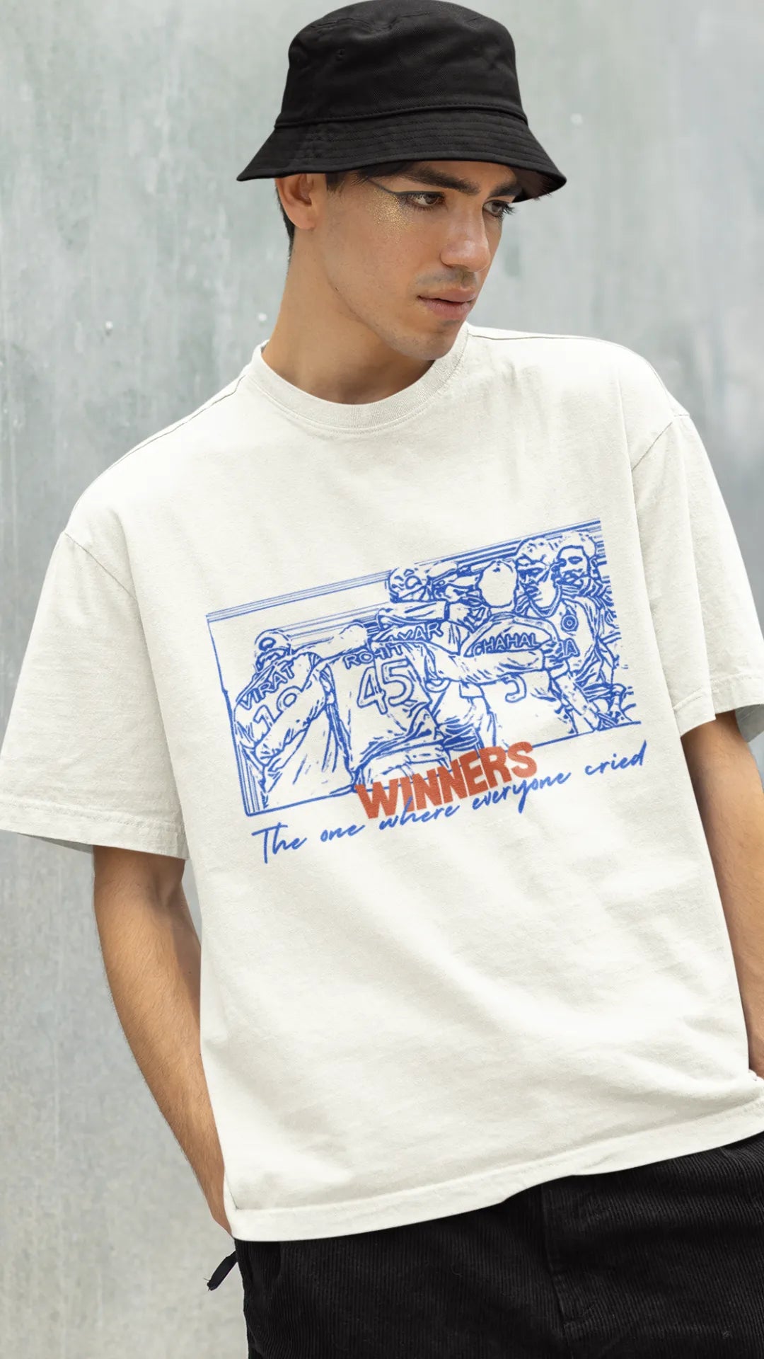 Left side view of a male model wearing an of-white oversized t-shirt featuring a design of the Indian cricket team in a celebratory huddle with the text "Winners" above them. Ideal for Indian cricket fans commemorating their team's World Cup victory.