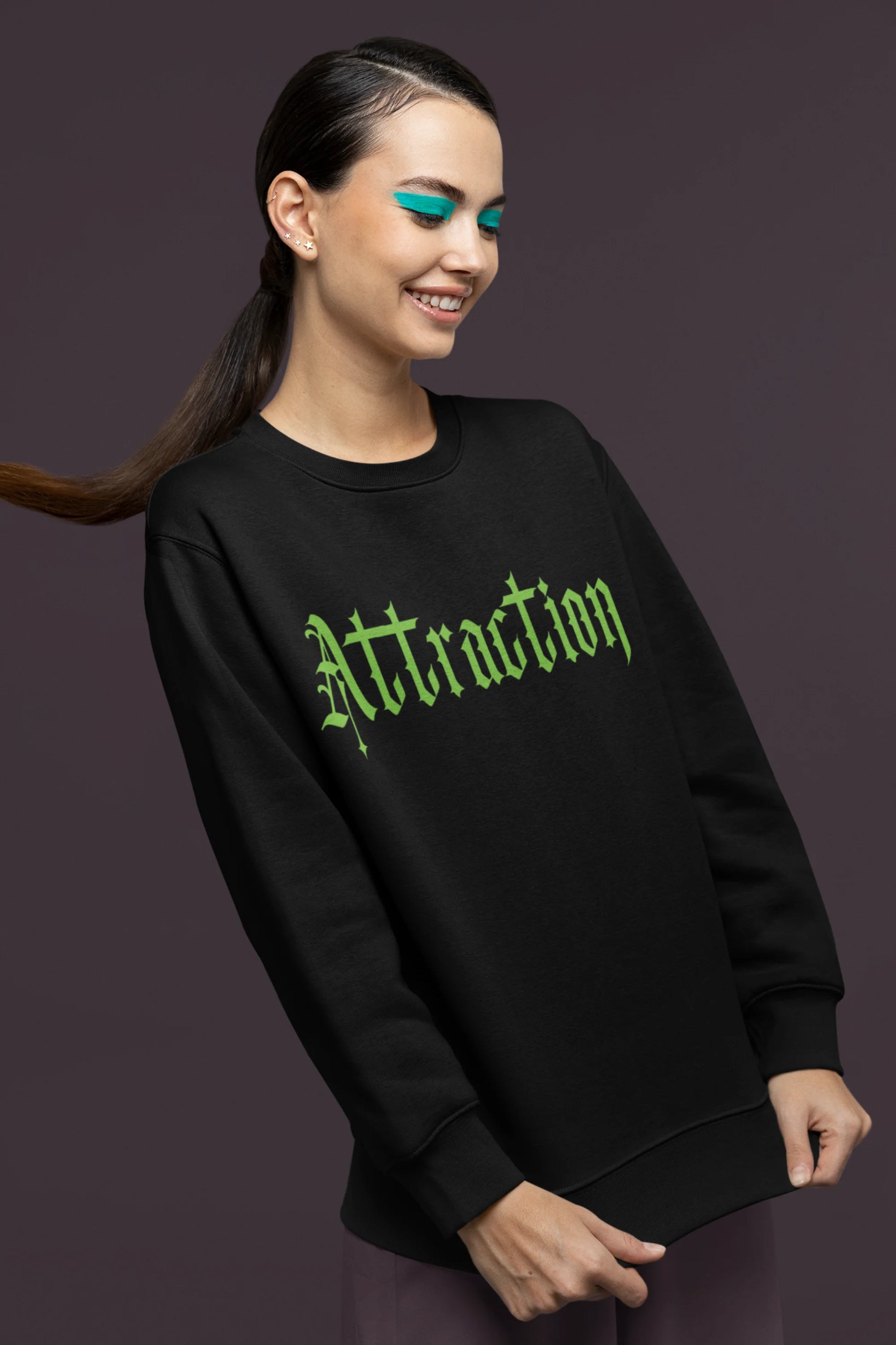 Second front view of a female model wearing a black sweatshirt with a brutalist design featuring two statues kissing and the word "Attraction".